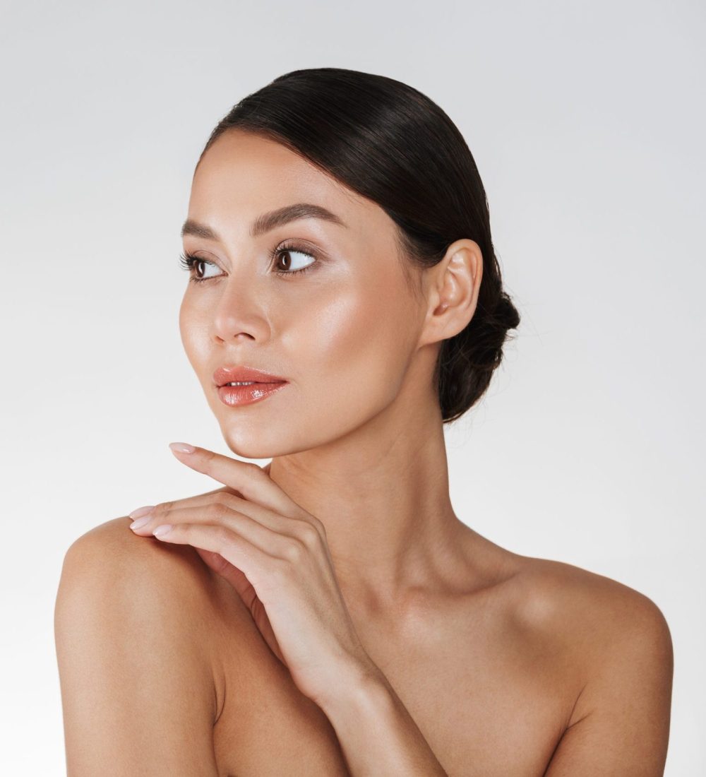 Beauty portrait of feminine young woman looking away and touching her nude shoulder isolated over white background